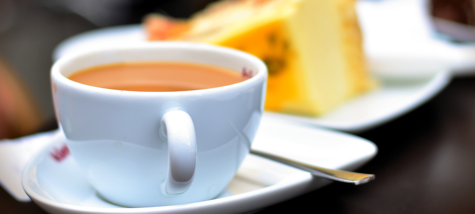 An image of a cup of tea and a piece of yellow cake
