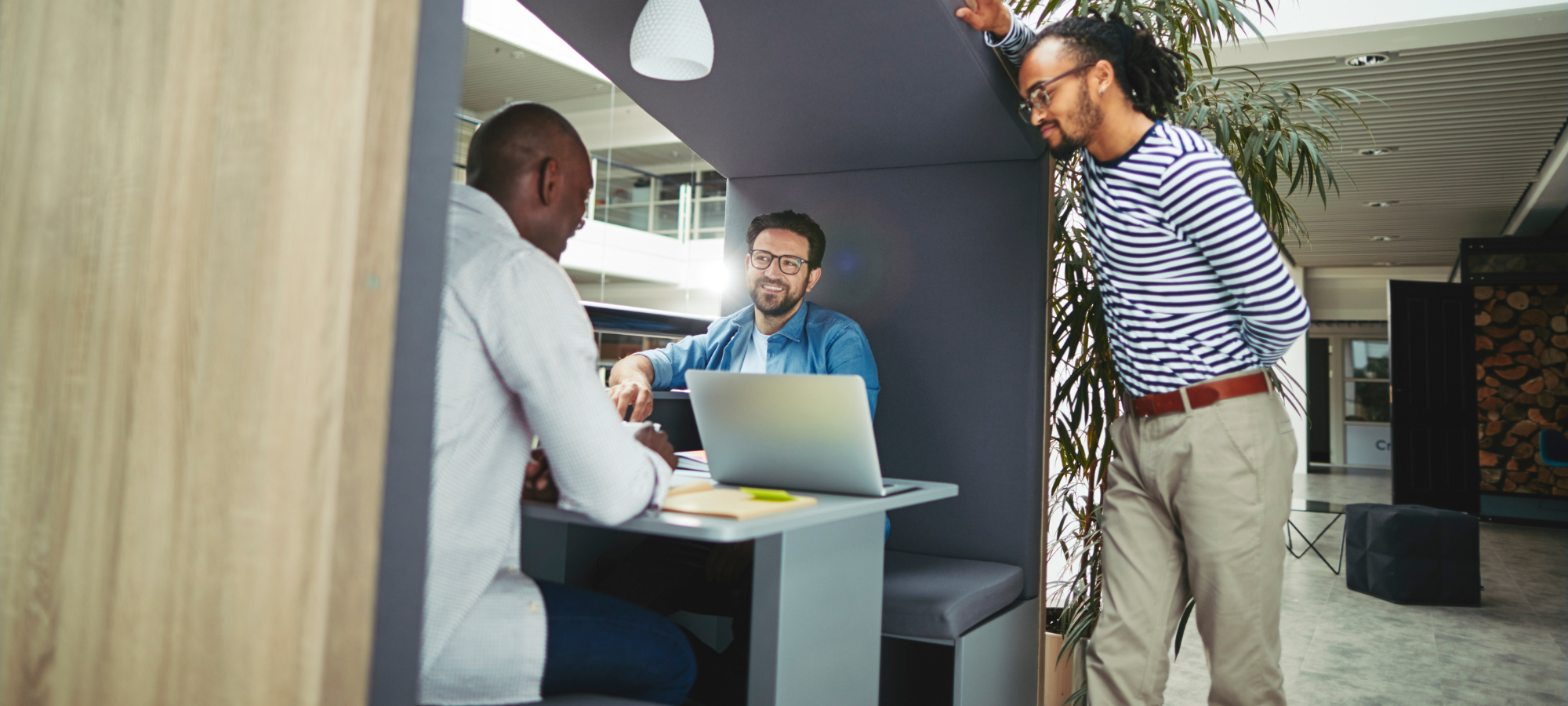 An image of three males working in an office meeting pod with a laptop.
