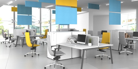 An office with white bench desks, grey and yellow task chairs and acoustics on the ceiling.