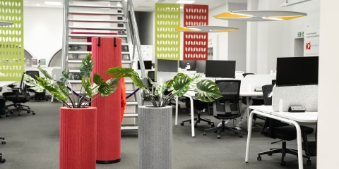 A modern office featuring a white, round acoustic pod, green planters, and a combination of grey and red acoustic panels and baffles on both the walls and ceiling.