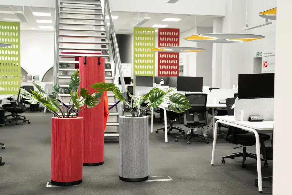 A modern office featuring a white, round acoustic pod, green planters, and a combination of grey and red acoustic panels and baffles on both the walls and ceiling.
