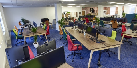 A large open office room with red and yellow chairs and wooden desks.