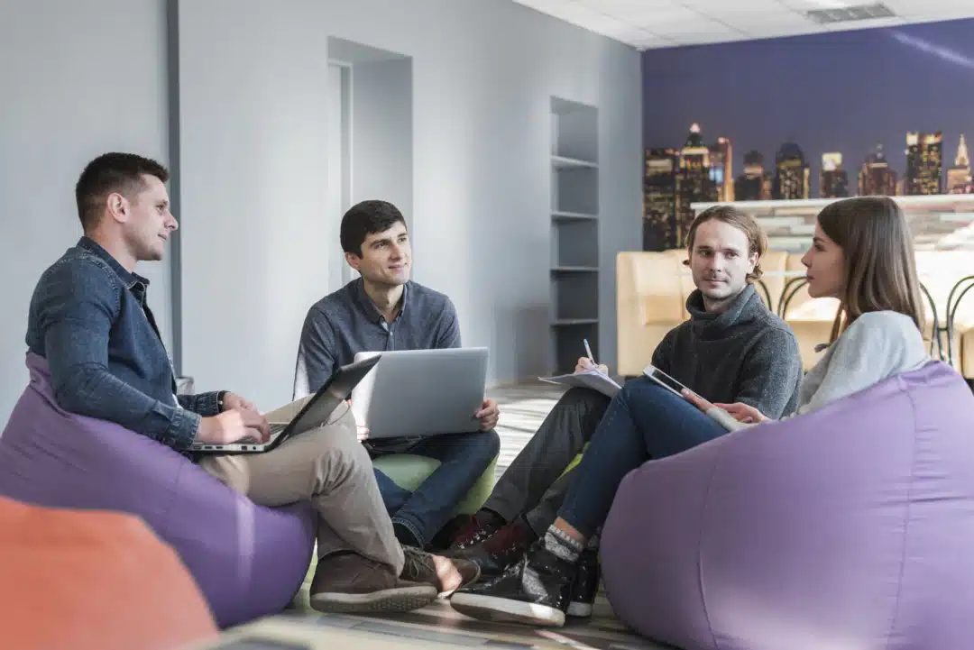 A group of people with laptops sitting on a purple bean bag chair.