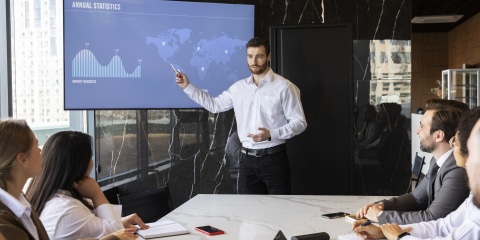 A group of people whoa are sitting at a meeting table watching a presentation.