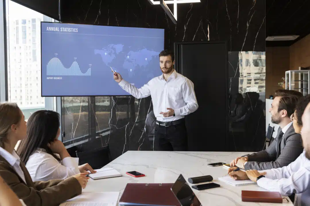 A group of people whoa are sitting at a meeting table watching a presentation.