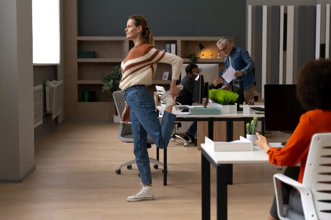 A woman in blue and stripe cream jumper stretching her leg in an office.