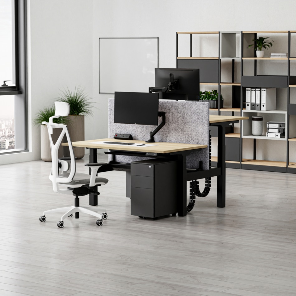 A single standing bench desk in a room with shelves in the background.