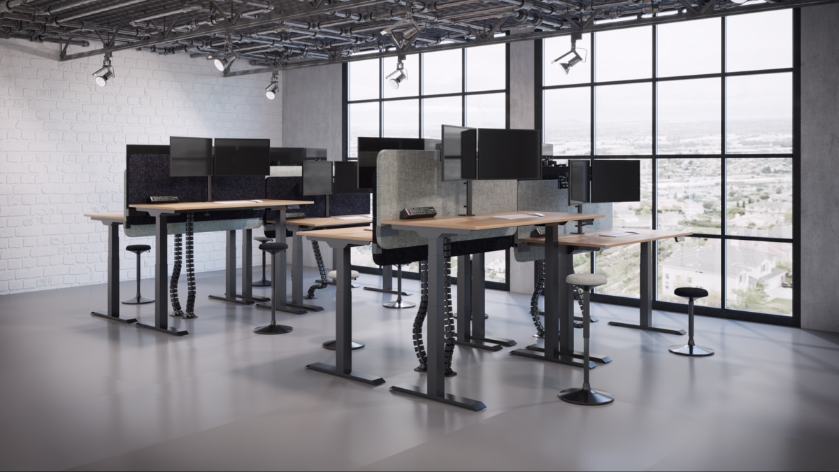 A large standing bench desks in a industrial style room with desktop screens placed on them.