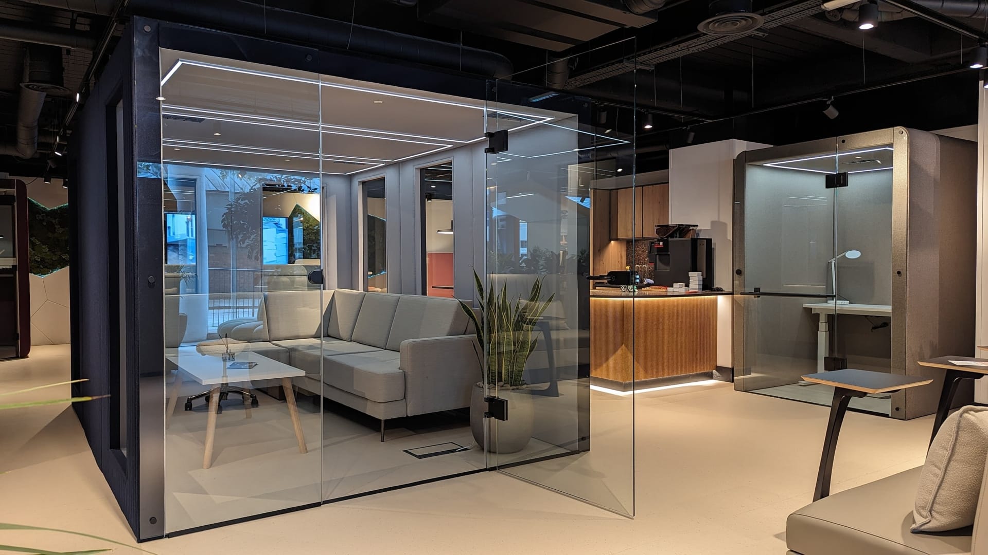 Acoustic square glass office pod with a sofa and a table in an office environment.