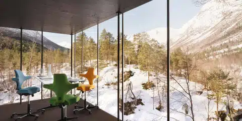 Several ergonomic chairs placed in the open room with wide glass window and snow,