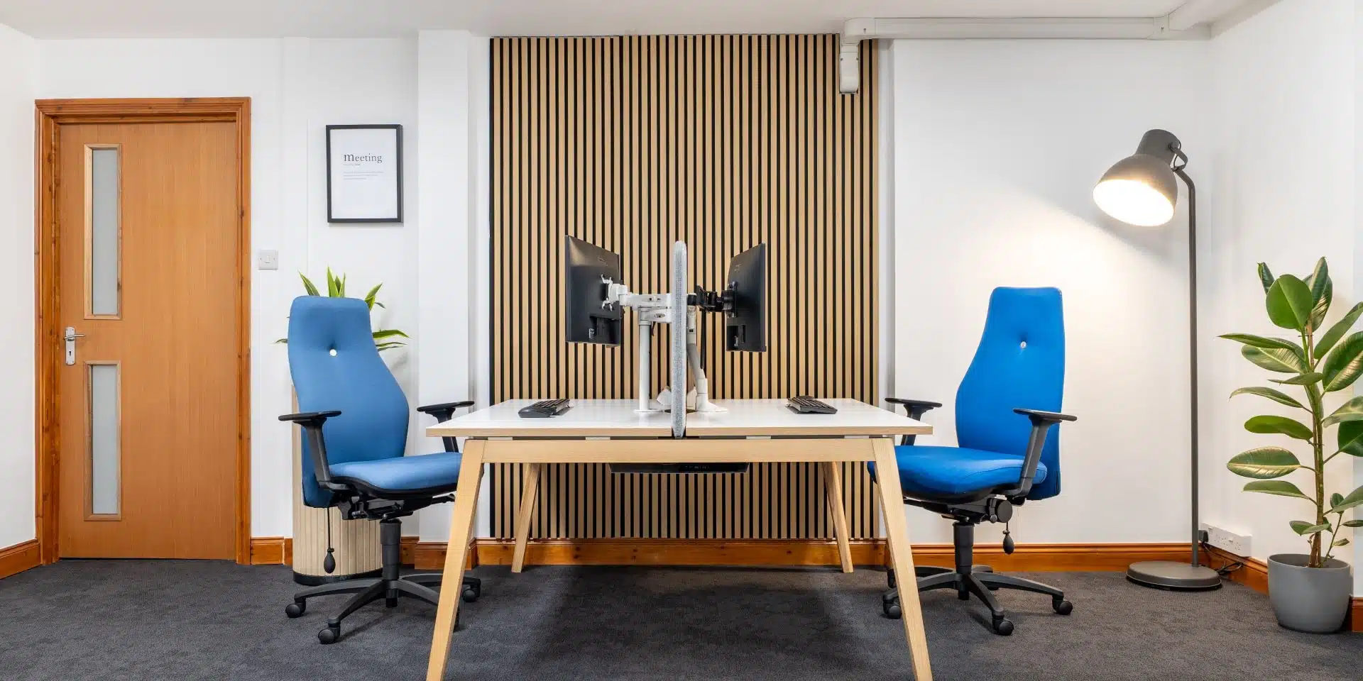 Two modern blue ergonomic office chairs positioned at a light wooden desk in a bright office environment.