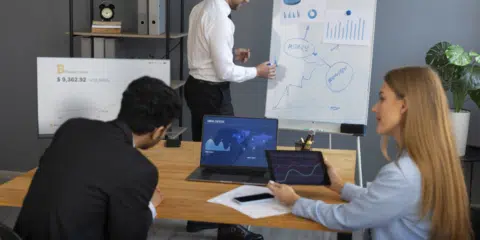 A group of business people who are in a meeting reviewing graphs on a laptop.