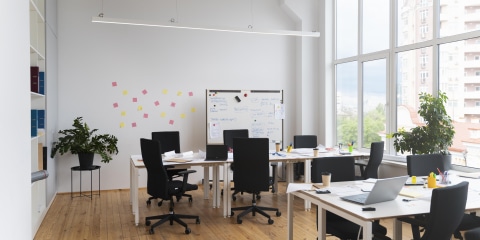 A small light room with office desks and chairs with a board in the background.