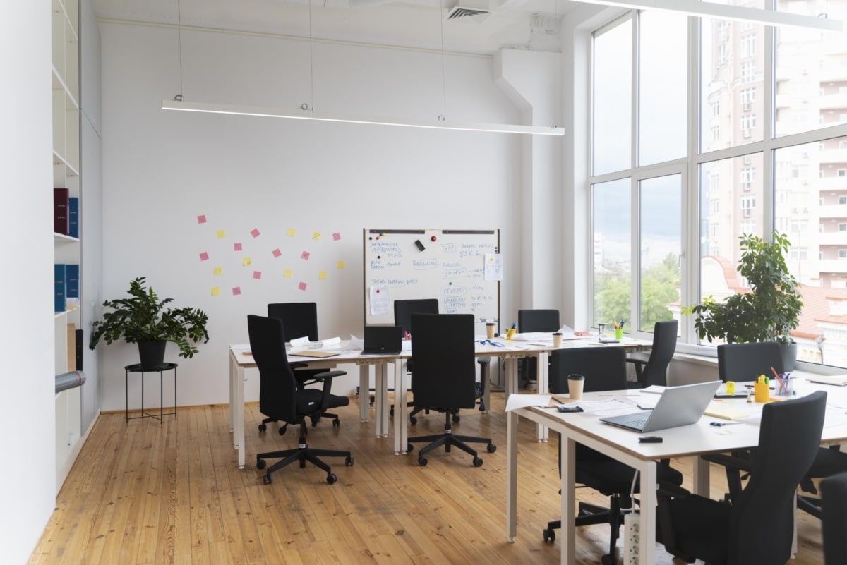 A small light room with office desks and chairs with a board in the background.