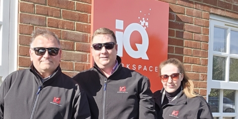A group of colleagues standing in-front of a iQ Brand board and a building outside.