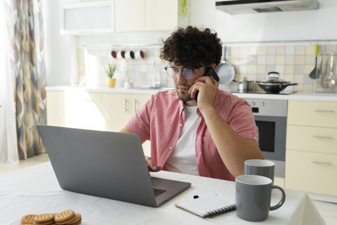 A male working from home in his kitchen talking on the phone.
