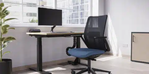 A black mesh chair with dark blue upholstery next to a single office deskl.