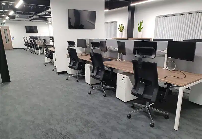 An office with several desks and black mech chairs.
