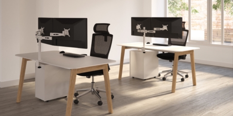 A wooden bench desk with black mesh office chairs.