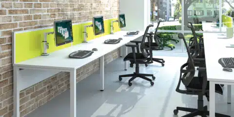 White bench style desks with yellow screen dividers in a open office space.