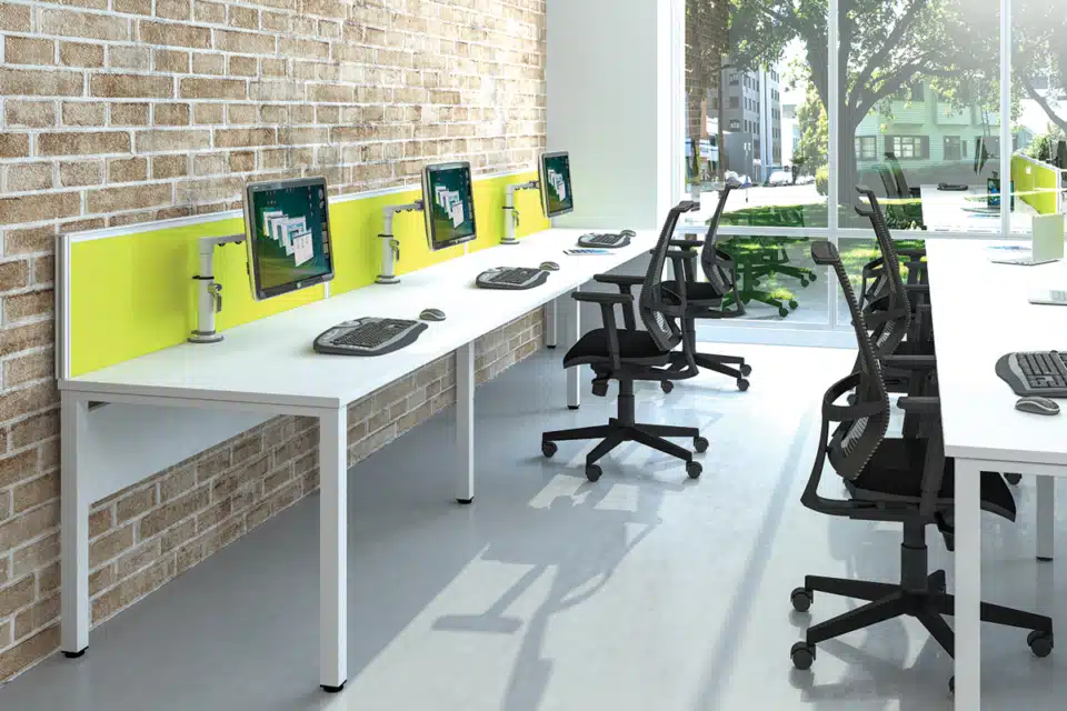 White bench style desks with yellow screen dividers in a open office space.