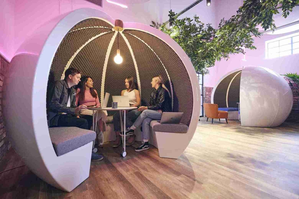 White round acoustic office pod with a team of happy colleagues inside having a casual discussion.