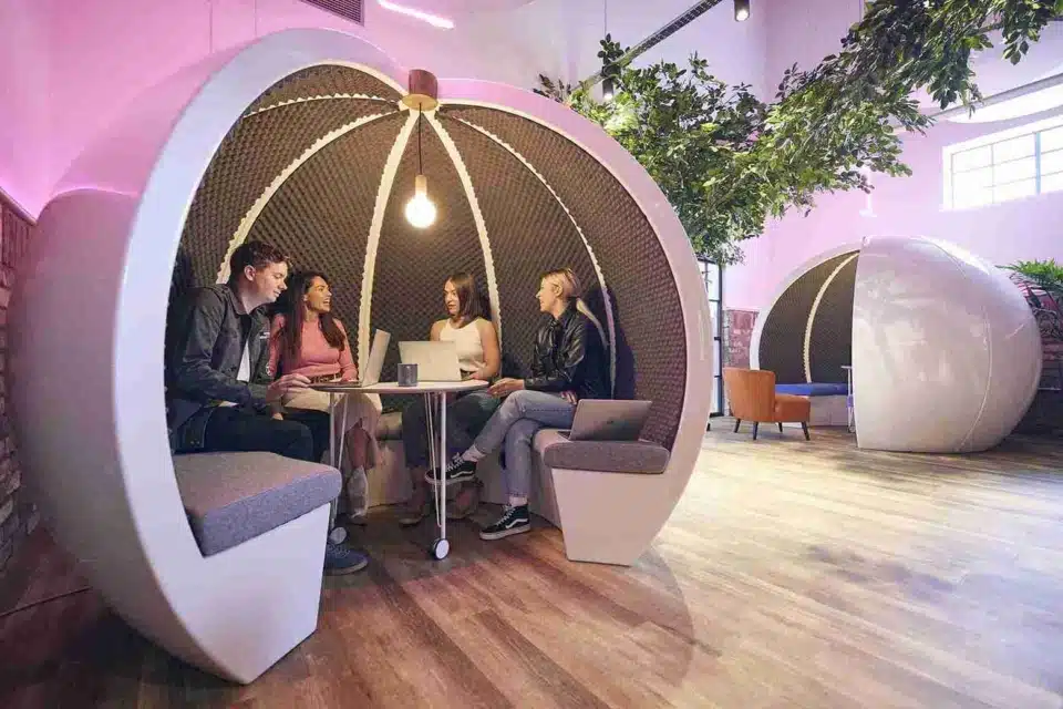 White round acoustic office pod with a team of happy colleagues inside having a casual discussion.