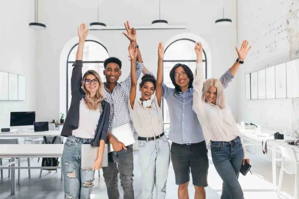 Diverse group of tired but happy employees laughing and smiling while celebrating the end of a successful project in their office.