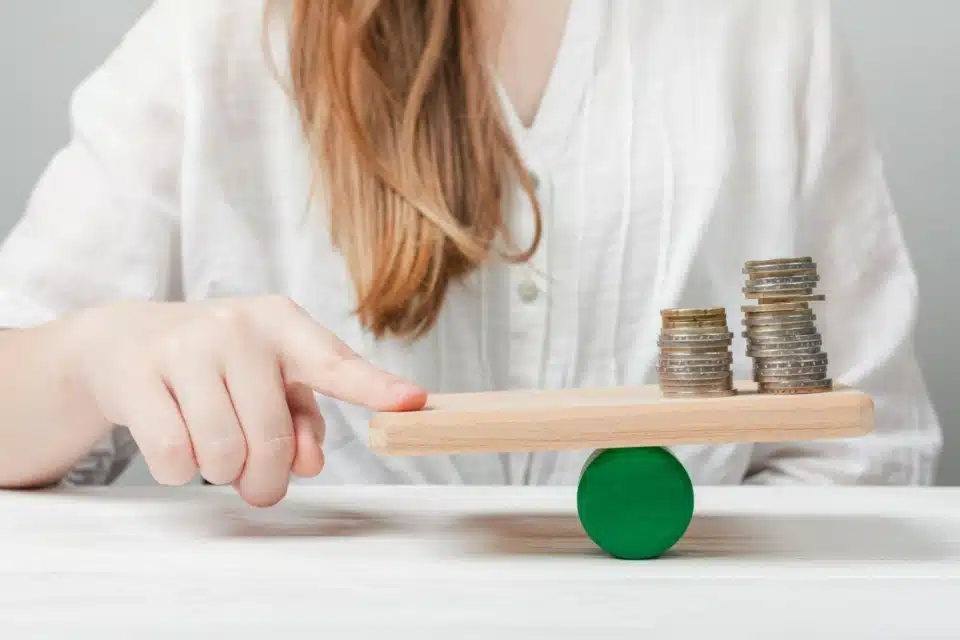 An image of a woman carefully balancing a stack of coins on her finger. The visual represents the delicate act of managing finances and working on a new project with a limited budget.