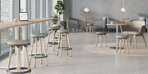 Two modern, high-legged stools with green and grey cushioned seats stand in a bright, open waiting room.