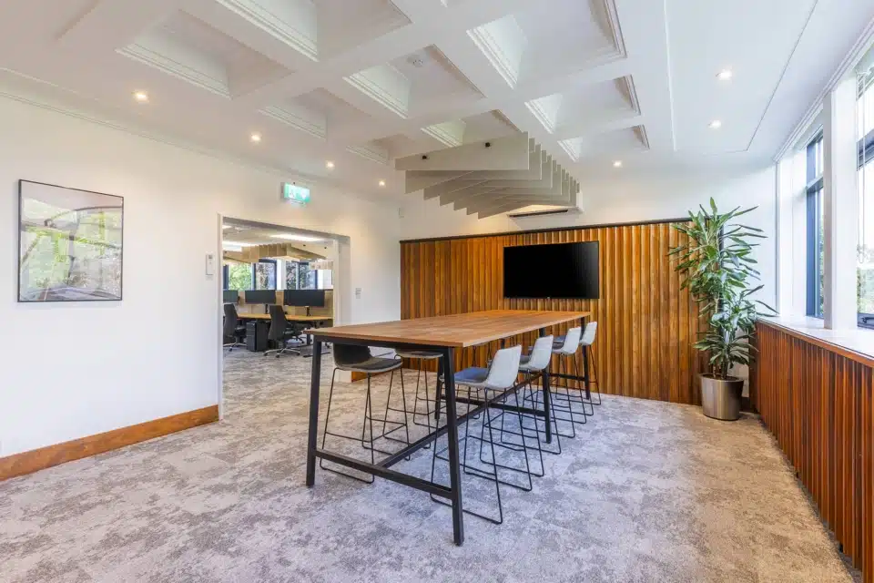 A high wooden table and chairs in a room with plants in the background.