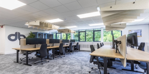 Black ergonomic chairs and wooden desks in a modern, spacious office with ceiling baffles.