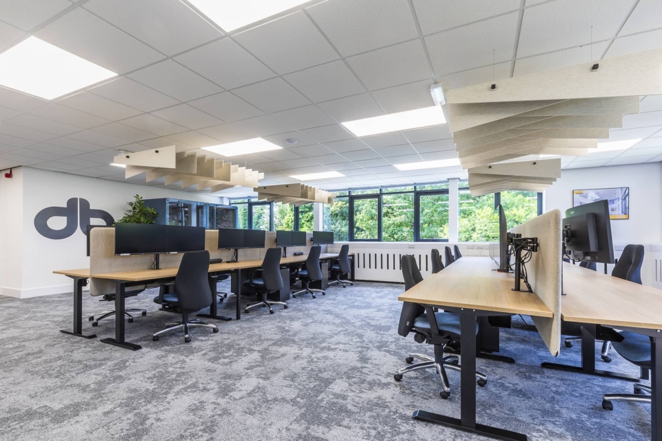 Black ergonomic chairs and wooden desks in a modern, spacious office with ceiling baffles.