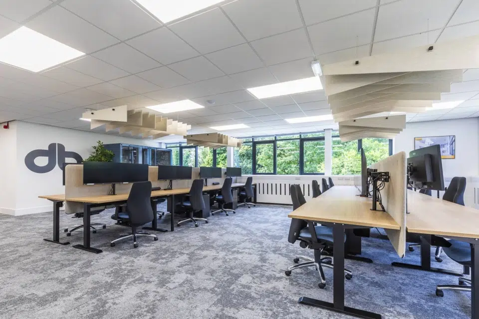 Black ergonomic chairs and wooden desks in a modern, spacious office with ceiling baffles.
