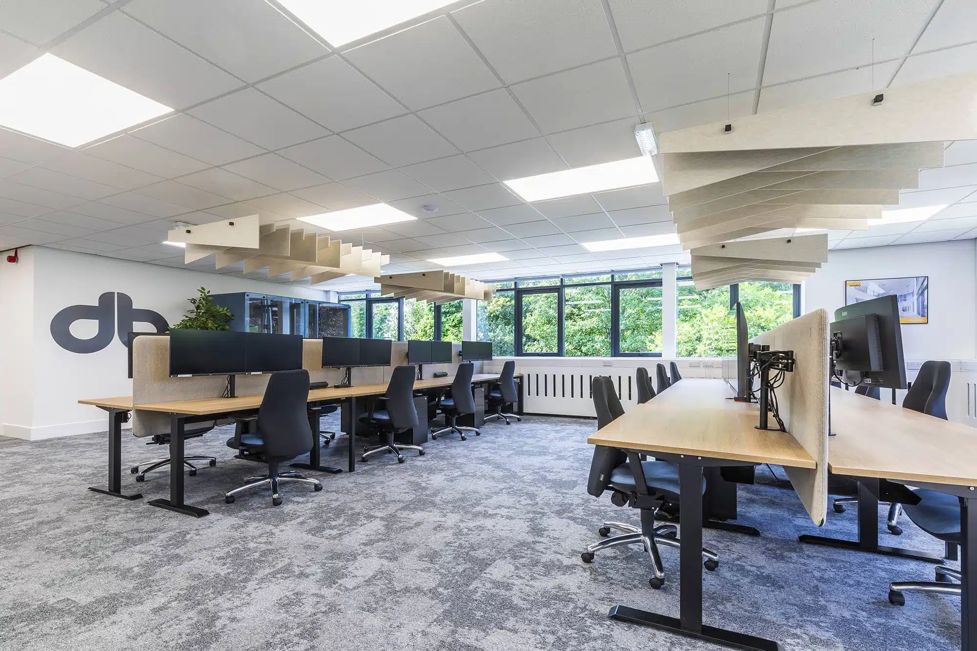 Black ergonomic chairs and wooden desks in a modern, spacious office with ceiling baffles.