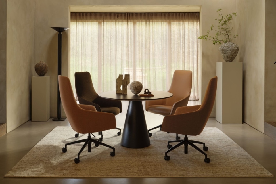 Four mid-century modern style swivel chairs around a large boardroom table on a neutral rug.