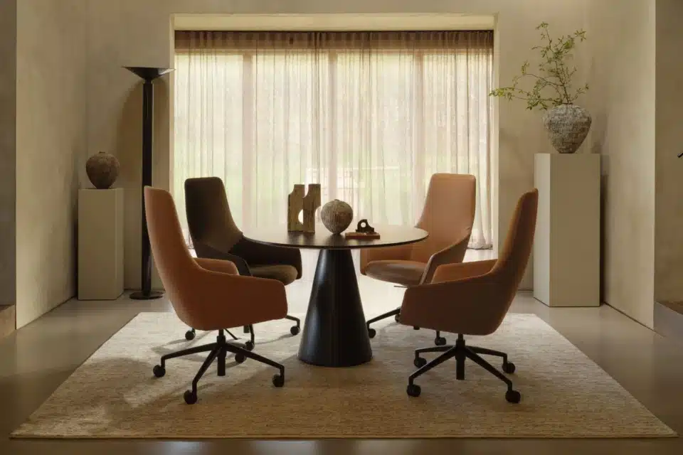 Four mid-century modern style swivel chairs around a large boardroom table on a neutral rug.