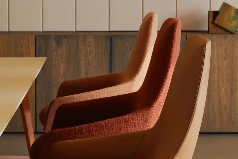 Three contemporary swivel chairs with warm-toned upholstery around a black round table in a high-end interior.