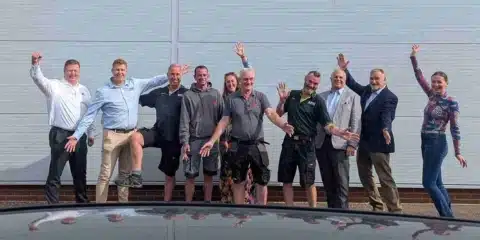 A happy, diverse group of team members from iQ Workspace and Tick Solutions laughing and playfully posing together in a bright, modern office space, celebrating the successful integration of the two companies.