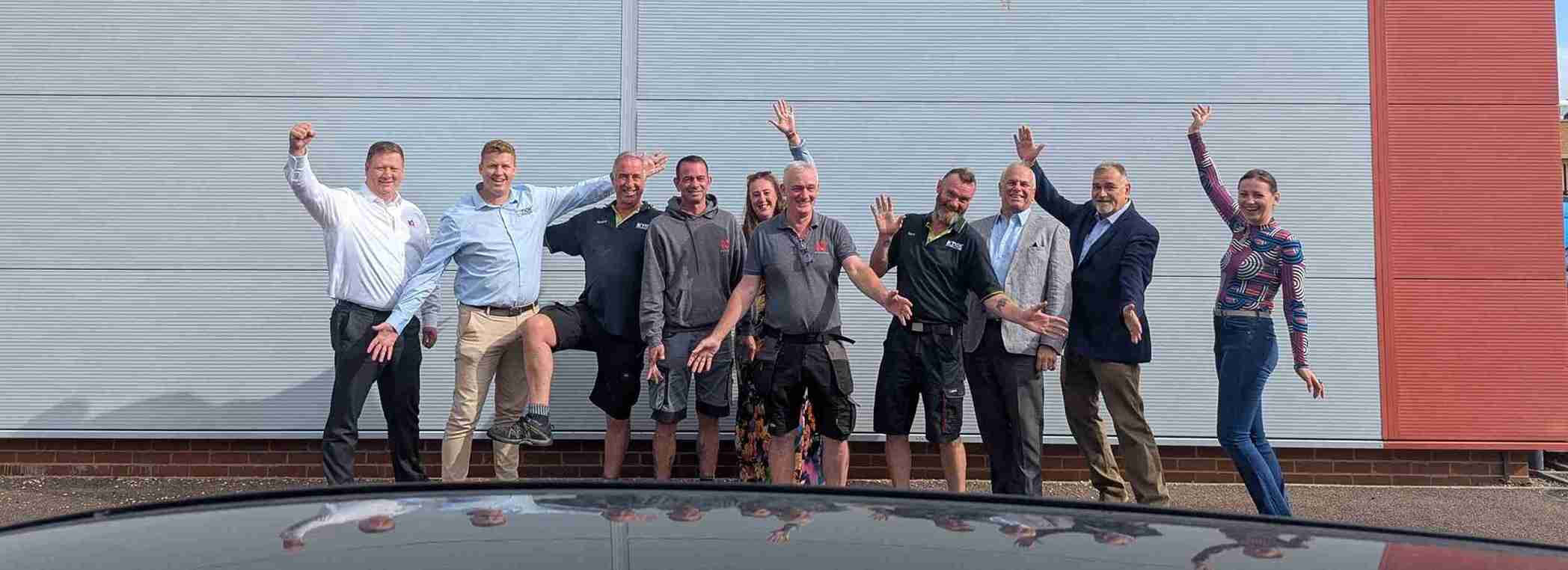 A happy, diverse group of team members from iQ Workspace and Tick Solutions laughing and playfully posing together in a bright, modern office space, celebrating the successful integration of the two companies.