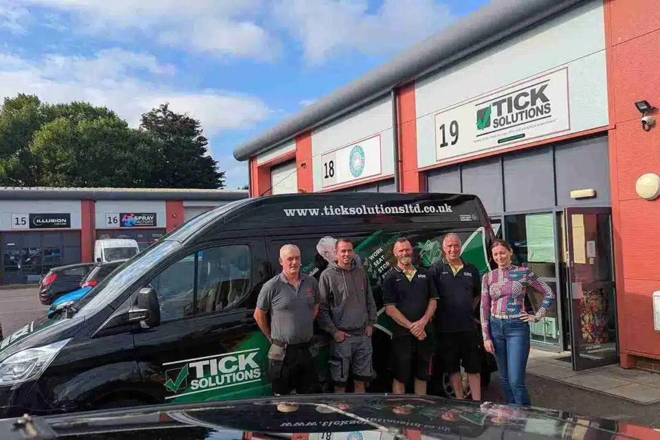 A happy team from Tick Solutions, standing and smiling in front of their company van on a sunny day.