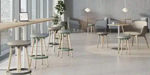 Two modern, high-legged stools with green and grey cushioned seats and light wooden legs stand in a bright, open waiting room.