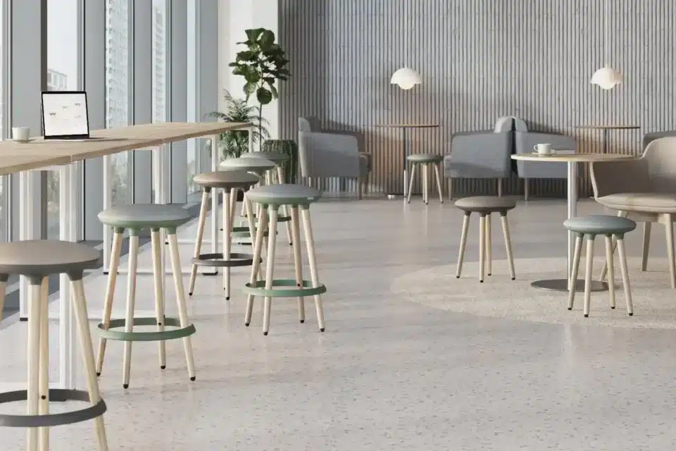 Two modern, high-legged stools with green and grey cushioned seats and light wooden legs stand in a bright, open waiting room.