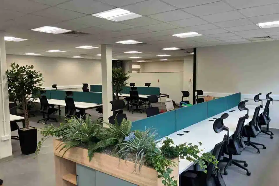 Modern, tidy office interior with white desks, turquoise dividers, and biophilic plants. A Nestlé logo is on the wall.