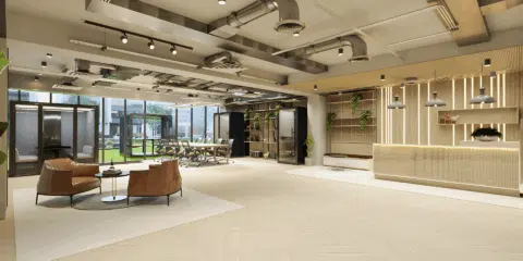 A modern open-plan office featuring a long light-wood communal table with ergonomic chairs and several sleek acoustic indoor work pods in the background.