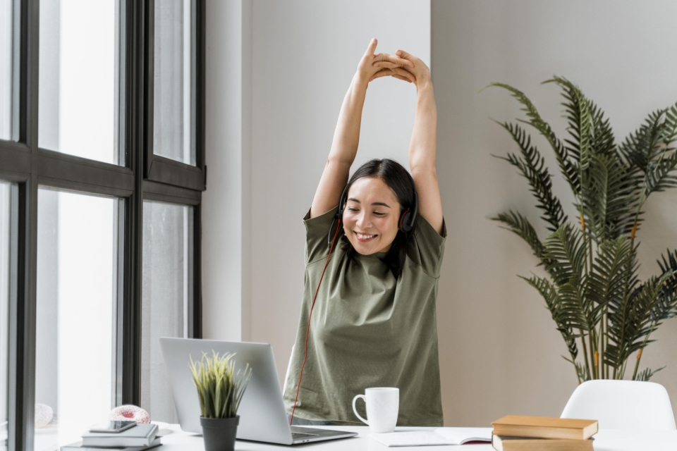 Woman Stretching at Desk with Headphones and Laptop.
