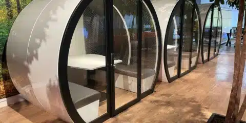 Three indoor meeting pods with glass placed in an open office.