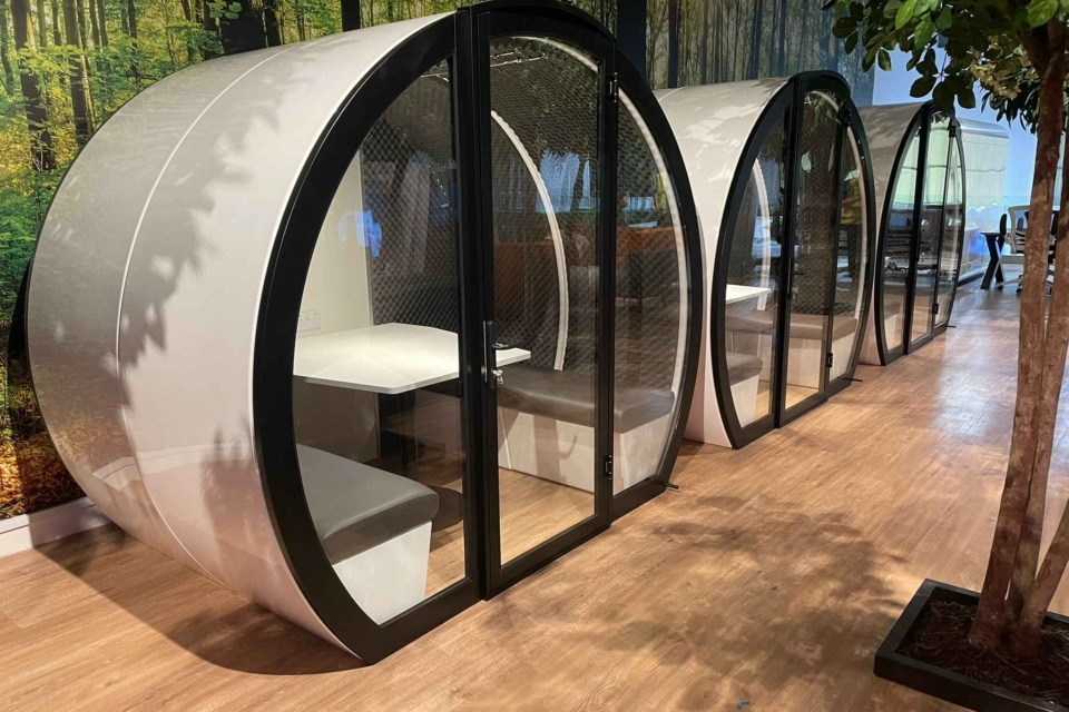 Three indoor meeting pods with glass placed in an open office.