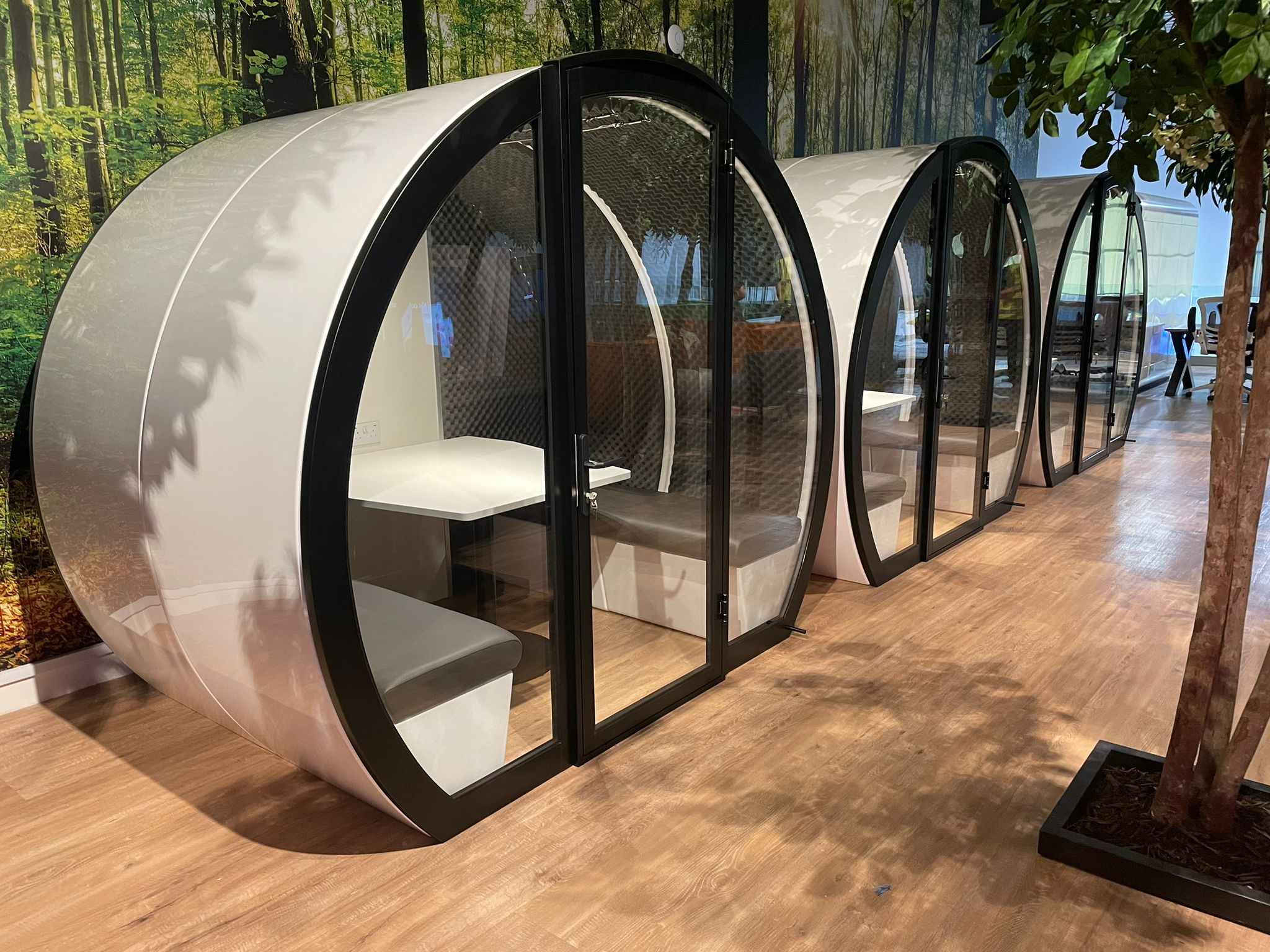 Three indoor meeting pods with glass placed in an open office.