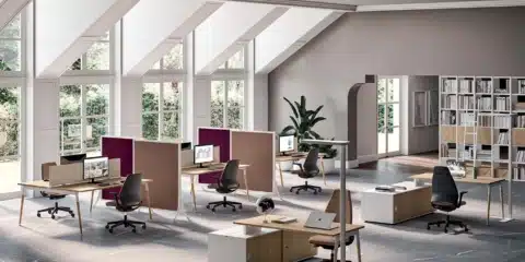 Collaborative X3 desks in a bright room with screens and divider panels.